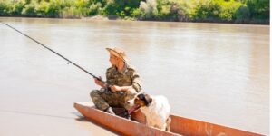 Man fishing from a small boat with his dog on a calm river in Venice, LA.
