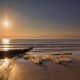 Lone fisherman casts a line from a boat on a calm, misty lake as the sun rises, creating a golden glow on the water, repre...