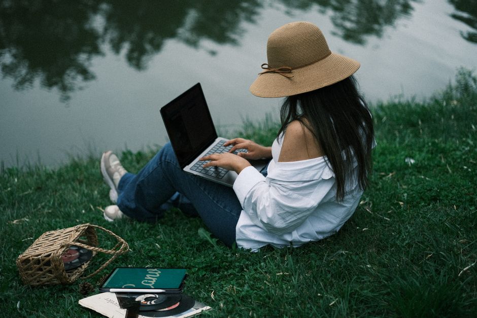 A person sits on a wooden dock with a laptop, planning their finances with a beautiful view of boats on the water in the background, illustrating the concept of monetizing a passion.