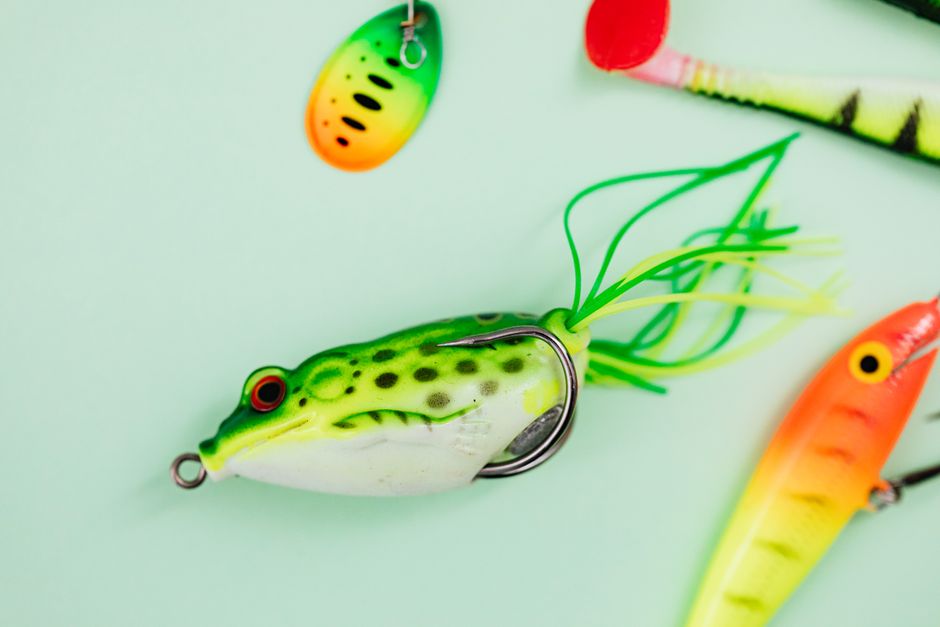 A colorful fishing lure rests on a bright wooden dock next to calm water, representing the tempting but costly bait of traditional 6% commission fees.